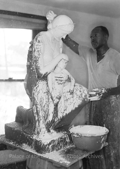 Black and white photo of an African American artist  in a studio covering a  figurative sculpture with plaster.